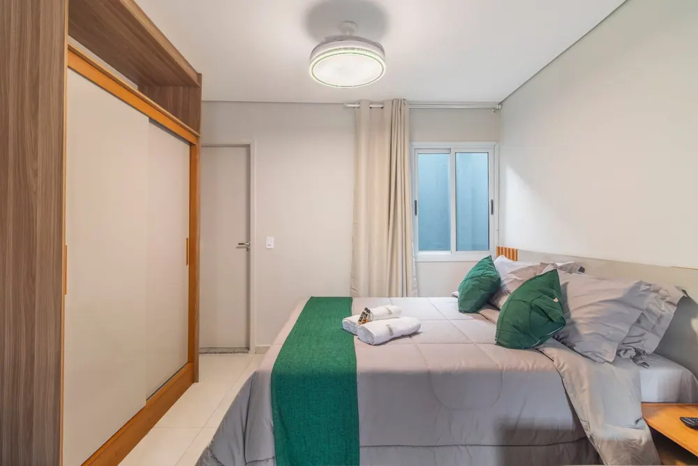 Quarto com cama de casal, almofadas verdes e toalhas dobradas, na Freguesia do Ó