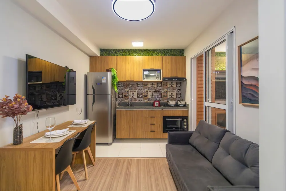 Sala com sofá cinza, mesa e cozinha de madeira, no apartamento de Guarulhos
