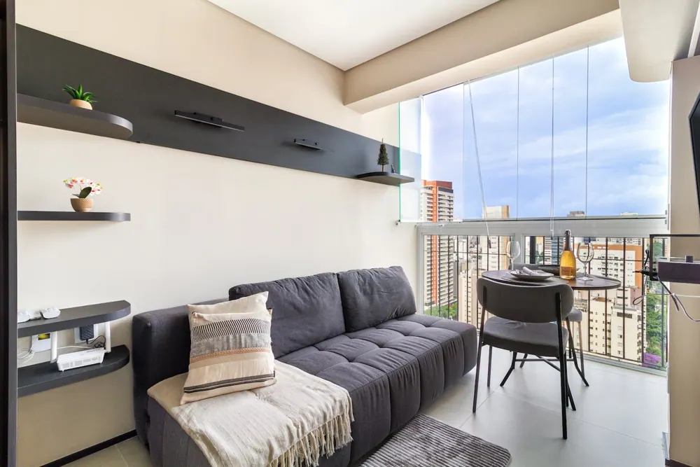 Sala com sofá cinza e varanda envidraçada com vista dos prédios da Vila Olímpia